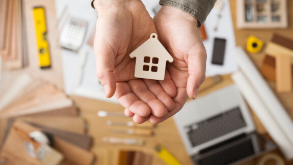 An image of someone holding a wooden keychain of a house