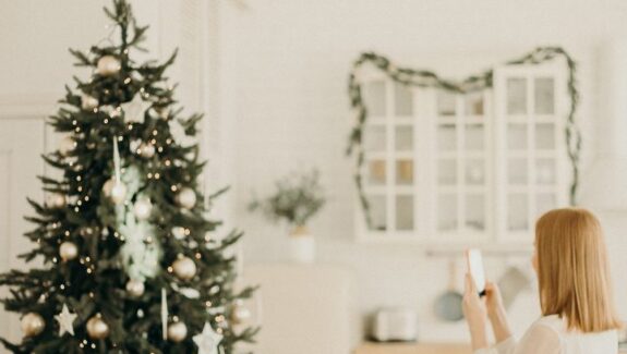 Image of a woman taking a photo of a christmas tree to share on social media. This can be a security breach at christmas time, as burglars can know where expensive gifts are kept under the tree.